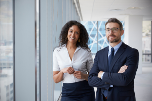 A man and a woman dressed professionally standing and smiling in a corporate office space