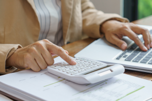 A person doing calculations on a calculator while simultaneously entering the information in their laptop